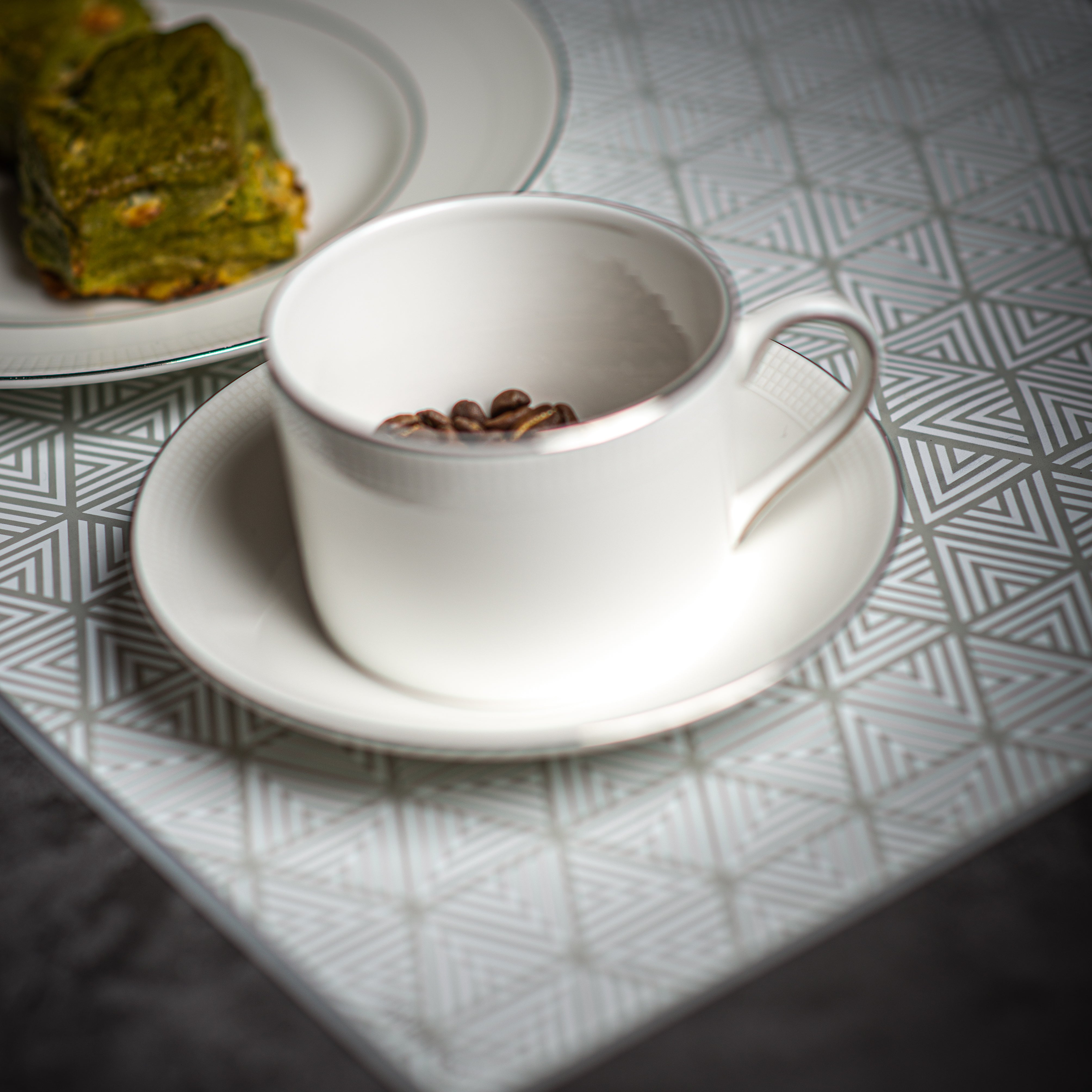 Coffee cup and plate on top of placemat with white and grey triangle pattern