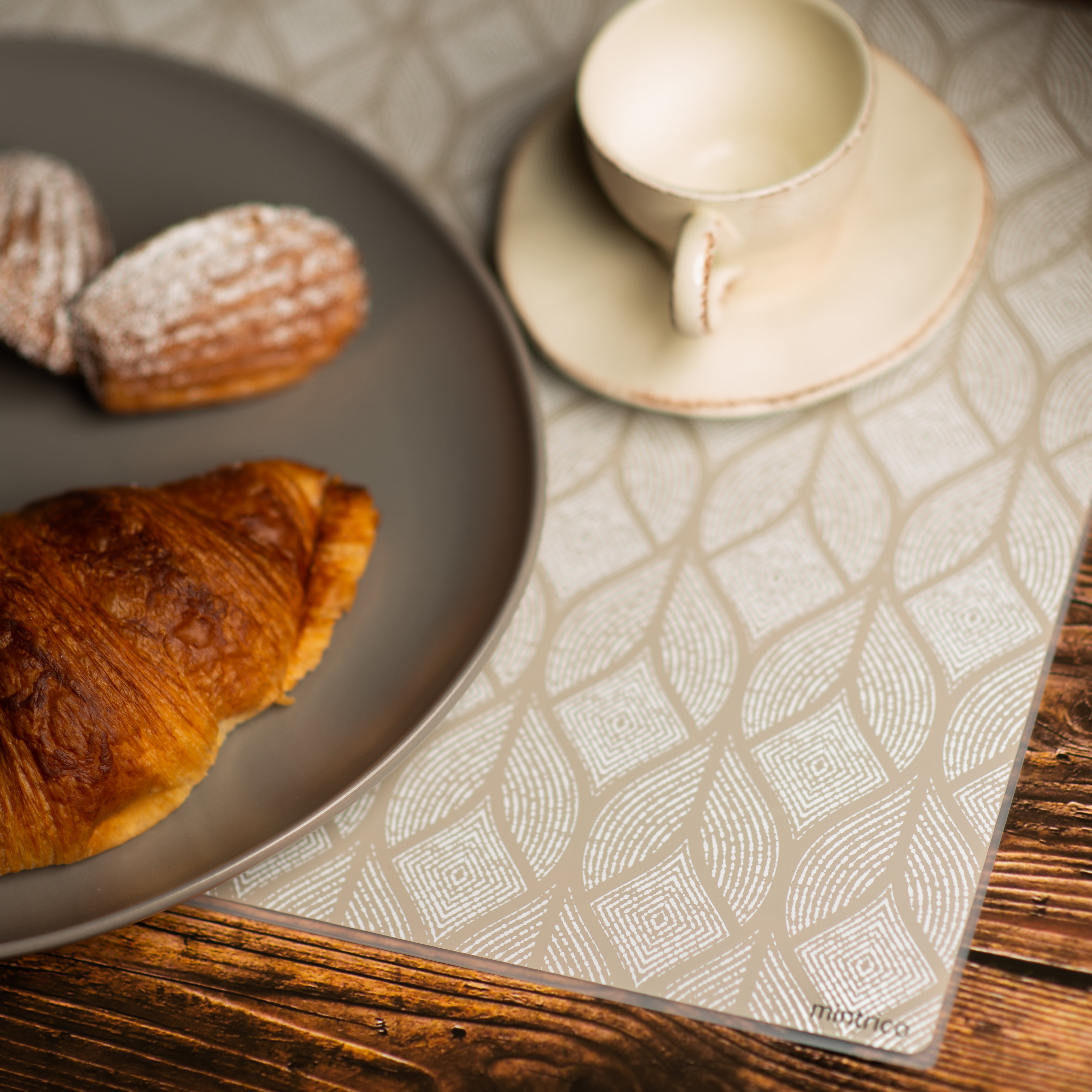 Baked goods and tea cup on silicone placemat with beige leaf pattern on wooden table