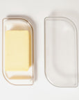 Stick of butter in butter dish with butter dish lid placed to the side on white background