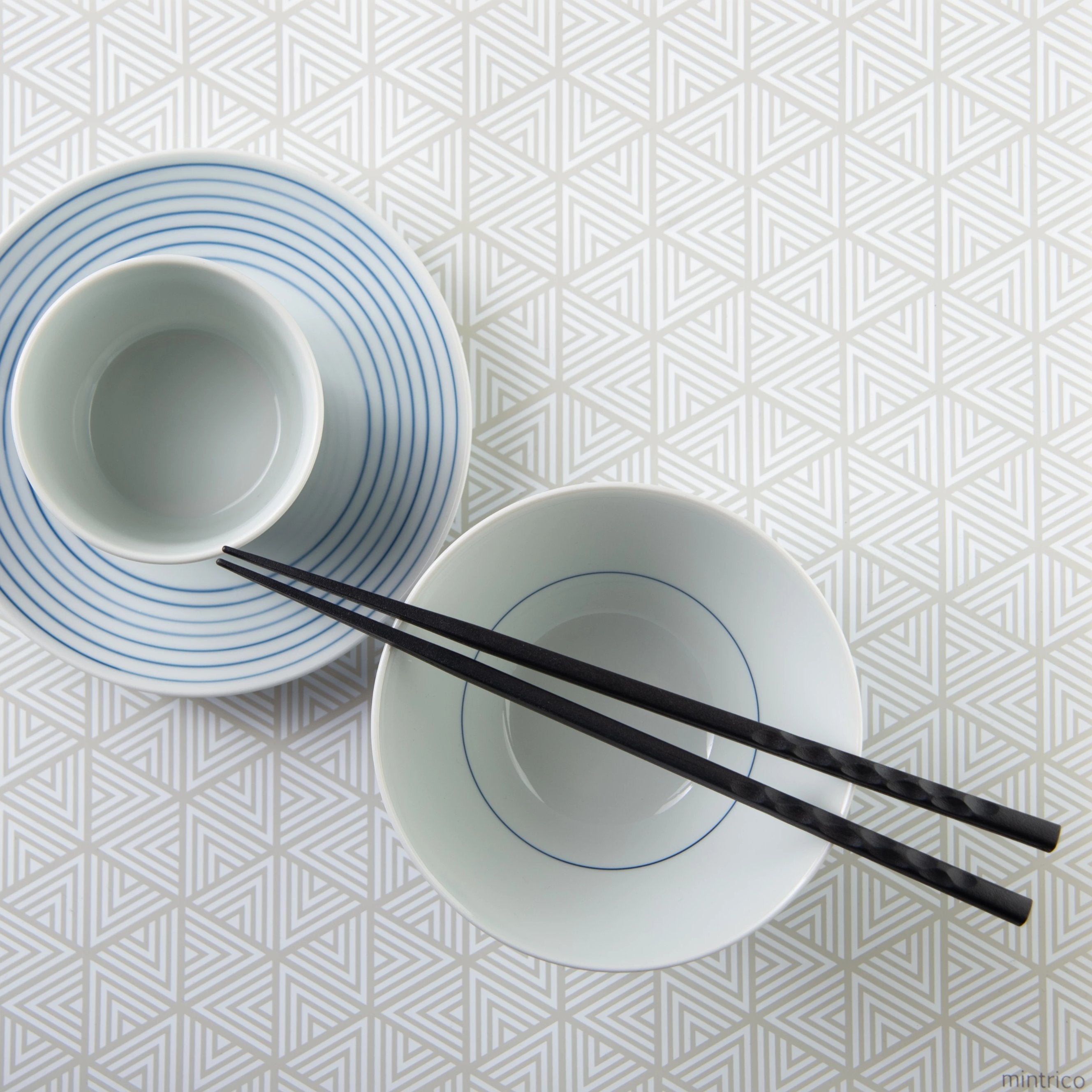 Chopsticks resting on top of bowl on placemat with white triangle pattern