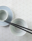 Chopsticks resting on top of bowl on placemat with white triangle pattern