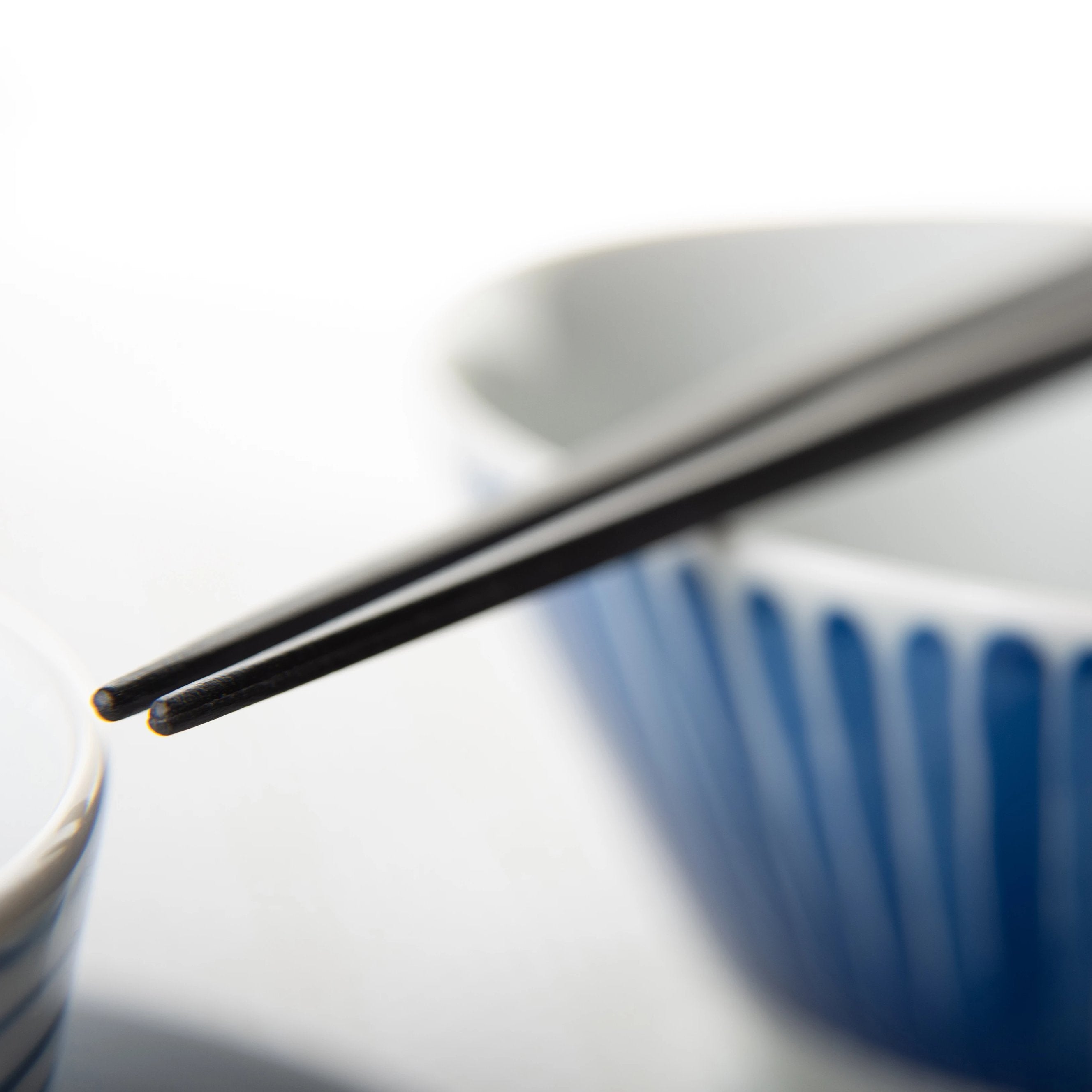 Close up of pair of chopsticks with sharp tips resting on top of a bowl