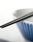 Close up of pair of chopsticks with sharp tips resting on top of a bowl